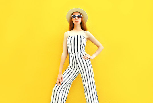 Fashion model woman is wearing a white striped pants, round hat colorful yellow background