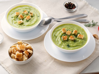 Two large white bowl with vegetable green cream soup of broccoli, zucchini, green peas on white background, side view