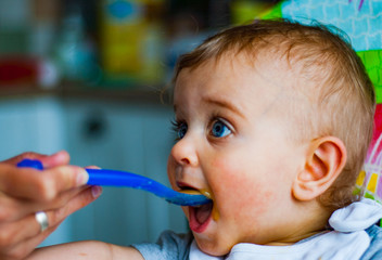 baby boy eating food with spoon at home