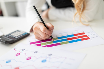 A young girl sits at a computer desk in the office, holds a pencil in her hand and works with charts and diagrams.