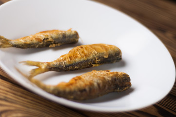 Row of three fried tasty fishes on white ceramic dish on old wooden rustic brown table