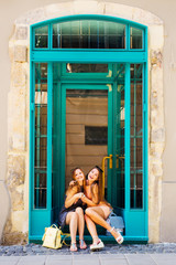 Girls sitting on the stairs near the door and hugging. At their feet are their backpacks