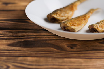 Row of three fried tasty fishes on white ceramic dish on old wooden rustic brown table with copy space for your text