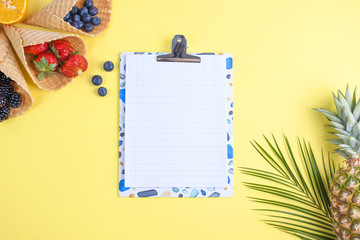 Tropical fruit is pineapple and palm branch on a yellow background, different sweet berries. White sheet for text in the center. Flat lay. Above. Copy space