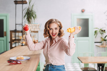 Pretty lady in shirt sitting with ketchup and mustard bottles in hands and joyfully looking in...