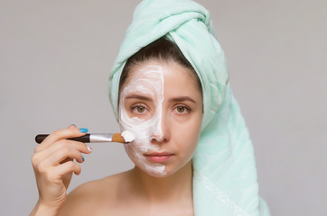 Serious woman applying a face cream by using a make up brush isolated on gray background. Face skin care treatment concept.