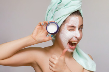 Woman holding in hand a jar with cream of facial mask and showing a thumbs up. Skin care treatment concept.