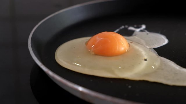 Close-up of breaking and dropping one egg in a frying pan for breakfast. Slow motion, 4k.