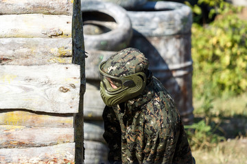 Paintball player in protective uniform and mask aiming gun in the forrest cover. A young man is preparing to shoot. The concept of active recreation, team play. Selective focus