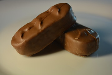 On a white glass plate there are beautiful candy bars of milk chocolate, two pieces