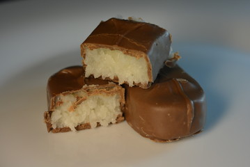 On a white glass plate there are beautiful sweets with coconut filling of white color and milk chocolate, pieces from a bar
