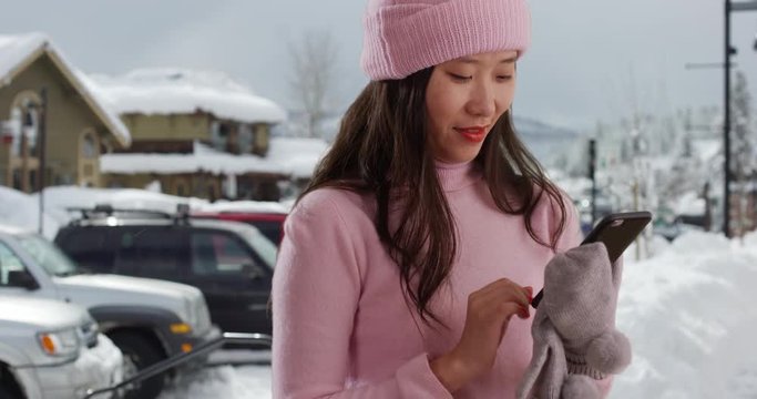 Happy millennial woman smiling and using smartphone to search online in snowy old town, Close up of cute young woman sending texts with cell phone on snow covered street, 4k
