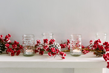 Red berry Christmas garland and votive candles on a mantlepiece. Copy space.