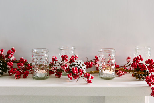 Red berry Christmas garland and votive candles on a mantlepiece. Copy space.