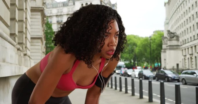 African American woman runner catching her breath and checking fitness tracker then running off screen, Black woman jogger resting on sidewalk with earbuds in then jogging away, 4k
