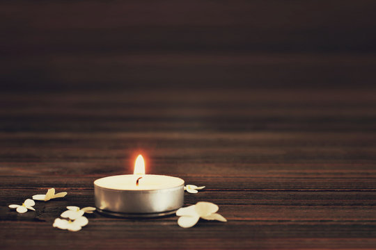 Burning candle and white flowers on wooden background