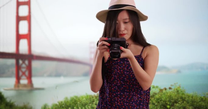 Portrait of lovely millennial photographer taking a picture with dslr camera in front Golden Gate bridge, Close view of young Asian woman taking a photograph in San Francisco California, 4k