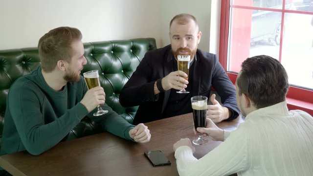 A company of handsome three male friends are talking and drinking beer. 4K