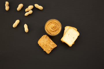 Toasts, unshelled peanuts and bowl of peanut butter on a black background, top view. From above.