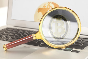 Magnifying glass with bitcoin inside on laptop with earth globe on screen