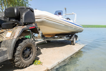 Transportation of inflatable boat on trailer. ATV quadbike moves ship to lake or river shore for launching. Beginning of water navigation and fishing season