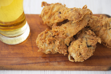 Fried chicken legs with sauce and cold beer on wooden board, side view. Closeup.