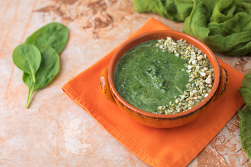 Cream of Spinach Soup in an Orange Bowl Topped with Chopped Pumpkin Seeds and Peanuts