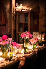 Table in dark room decorated with pink roses, peonies, and candles