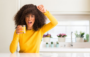 African american woman drinking orange juice in a glass annoyed and frustrated shouting with anger, crazy and yelling with raised hand, anger concept