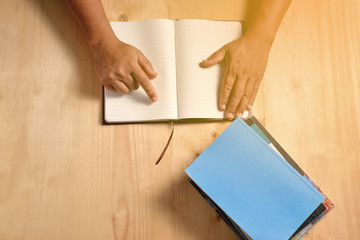 Human hands open blank notebook on the wooden table.