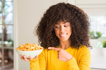 Fototapeta na wymiar African american woman holding a plate with potato chips at home very happy pointing with hand and finger