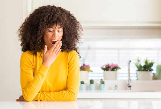 African american woman wearing yellow sweater at kitchen bored yawning tired covering mouth with hand. Restless and sleepiness.