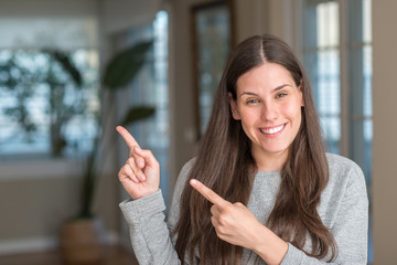 Young beautiful woman at home smiling and looking at the camera pointing with two hands and fingers...