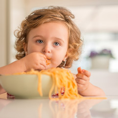 Close up of beautiful blond child eating spaghetti with hands at home.