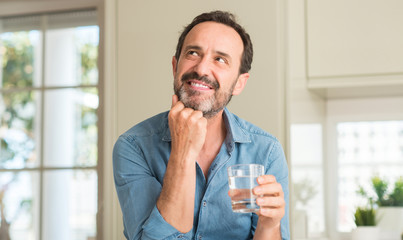 Middle age man drinking a glass of water serious face thinking about question, very confused idea