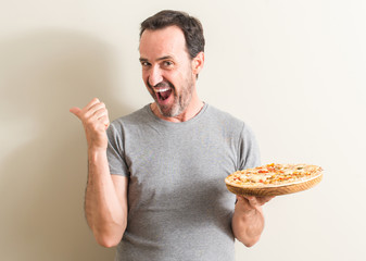 Senior man holding pizza pointing with hand and finger up with happy face smiling