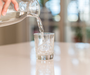 Closeup of bottle pouring watter in a glass on the table with sunny bokeh background at home.