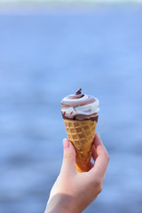 Ice cream cone in hand, chocolate ice cream on blurred background, milk dessert on summer vacation, blank for designer, copy space