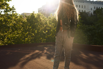Girl in leather jacket with hands in pockets in sunlight.