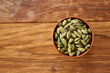 Green cardamon in ceramic bowl on rustic wooden background close-up, top view, selective focus.
