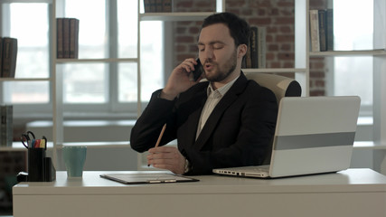 Successful young business man talking on cell phone at modern office