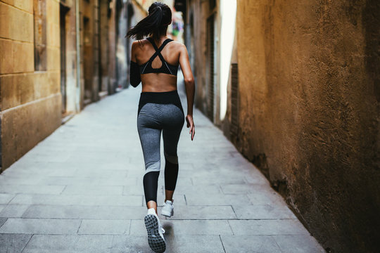 Back View Of A Young Woman Running On The Street. Urban Life.