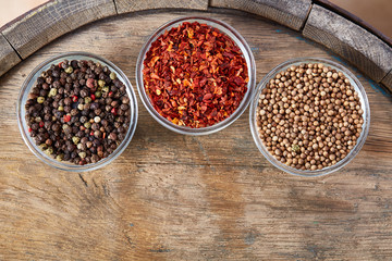 Glass bowls with various spicies on wooden barrel, top view, close-up, selective focus.