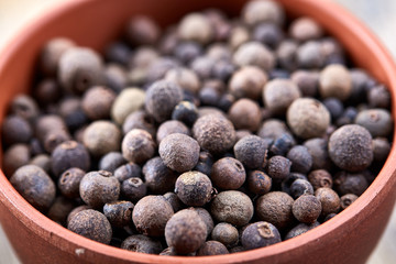 Close-up clay bowl with dried allspice berries on vintage wooden background, top view, macro, shallow depth of field.