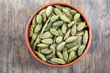 Green cardamon in ceramic bowl on vintage wooden background close-up, top view, selective focus.