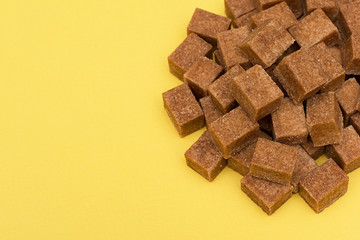 Brown sugar in cubes on a yellow background. An empty place to write a text.