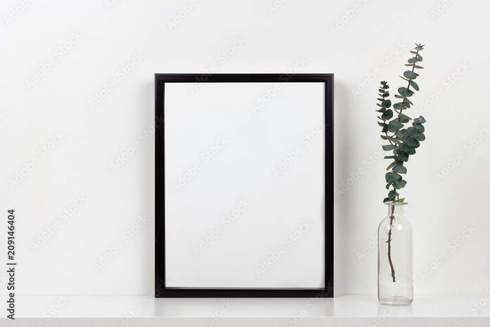 Wall mural Mock up black frame with vase of branches on a shelf or desk. White shelf and wall. Portrait frame orientation.