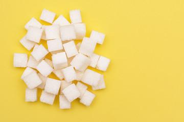 White sugar in cubes on a yellow background. An empty place to write a text.
