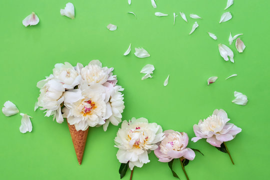 Ice cream cone with white peony flowers on green background. Summer concept. Copy space, top view