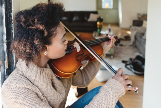 A young woman playing the viola at home